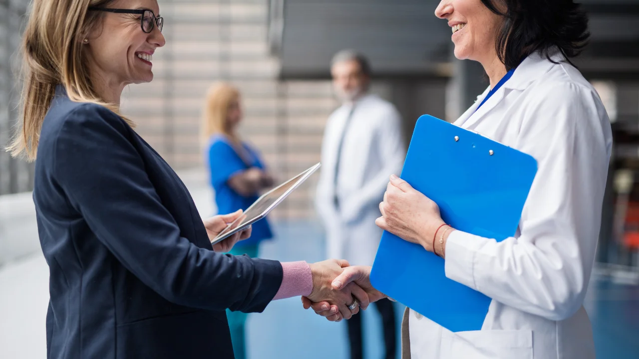 Representantes de una empresa de tecnología y un hospital estrechando manos en una reunión.